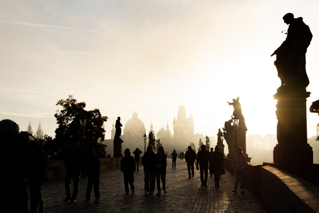 People walking on Charles Bridge in Prague during a sunny misty morning